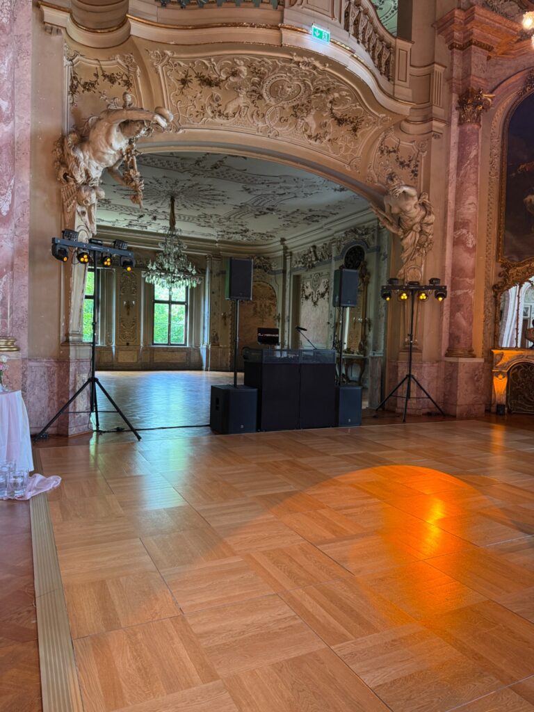 Lautsprecher und Lichttechnik vor einem DJ-Platz in einem festlichen Saal.